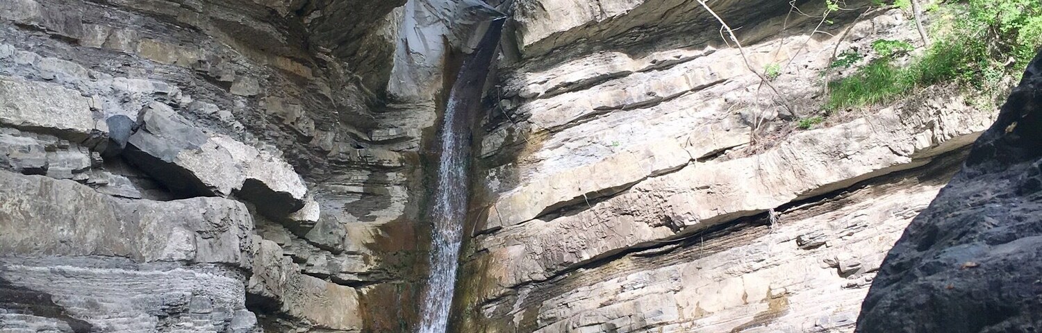 A waterfall cascading down a rocky cliff into a pool surrounded by large boulders and greenery.