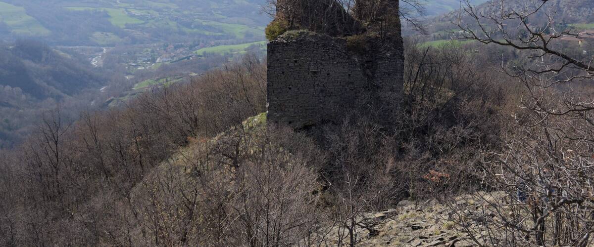 A ruined stone tower on a hill with a valley and mountains in the background.