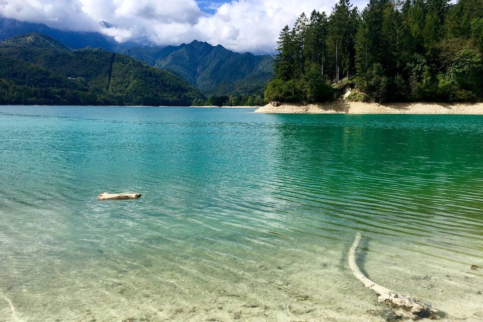 A clear lake surrounded by mountains and a forested area.