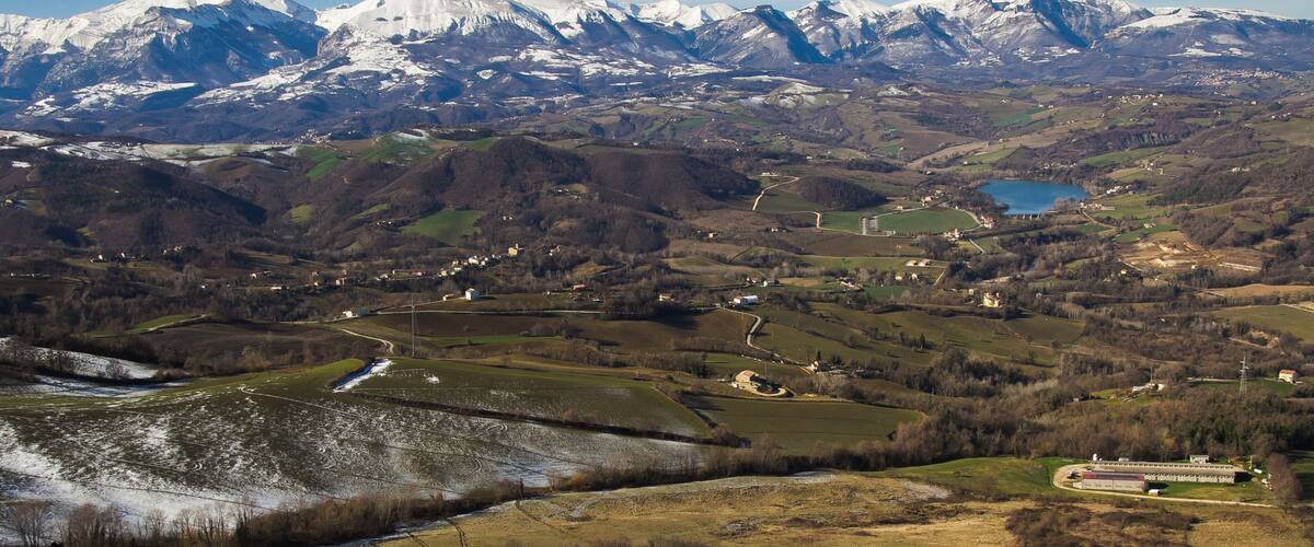 A mountainous landscape with snow-capped peaks, a river, and scattered buildings.