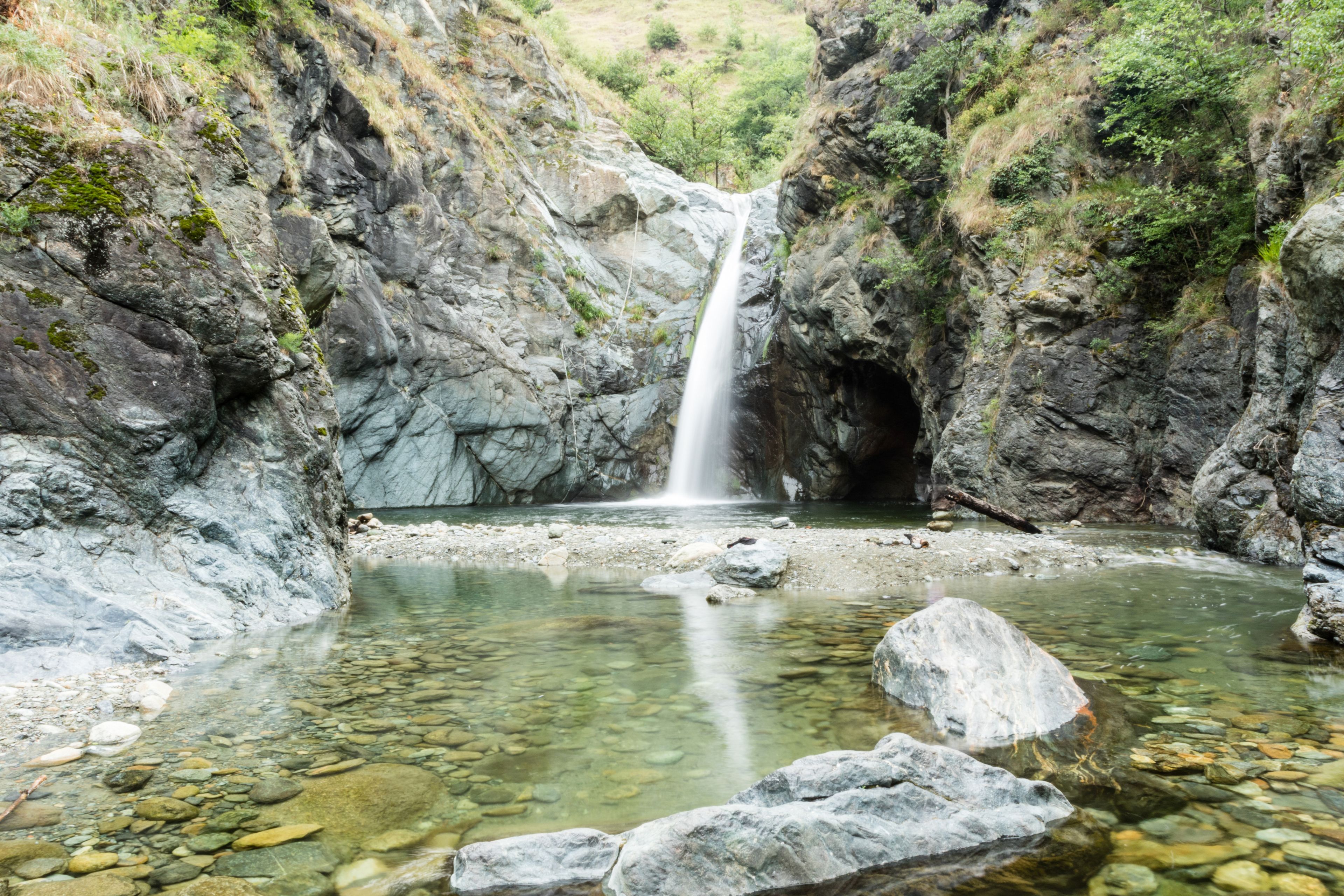Ein Wasserfall stürzt in ein klares Becken, umgeben von felsigem Gelände und Grünpflanzen.