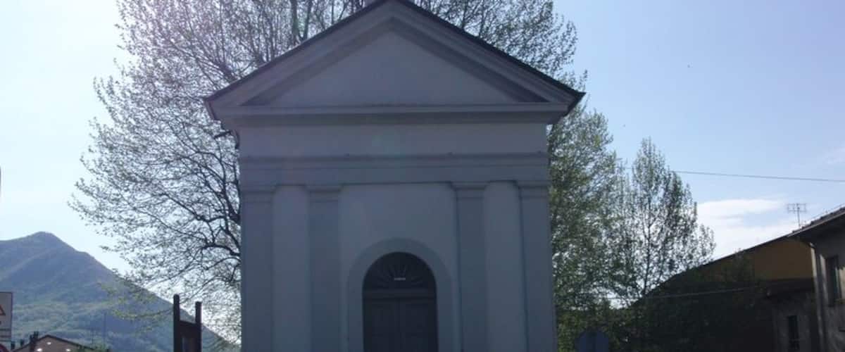 A small white church with a bell tower, surrounded by a metal fence and trees.