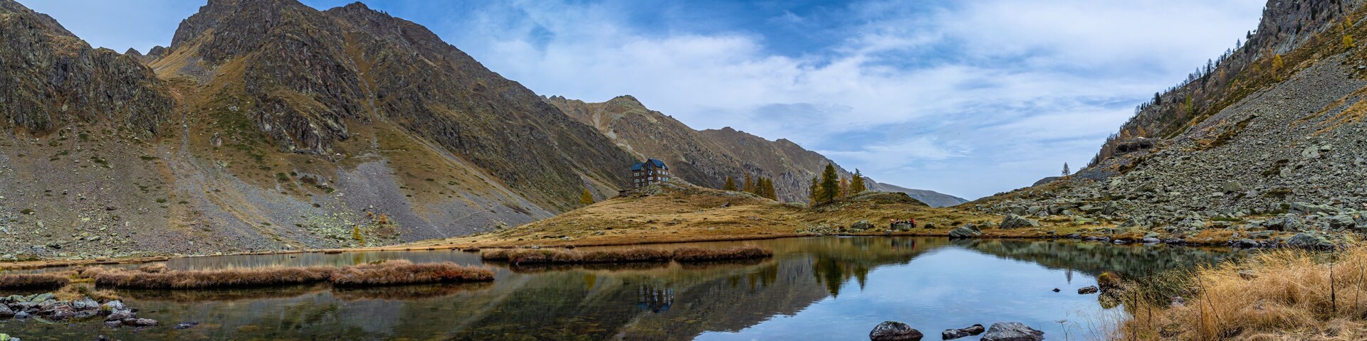 Un lago de montaña con terreno rocoso y un pequeño edificio en una colina.
