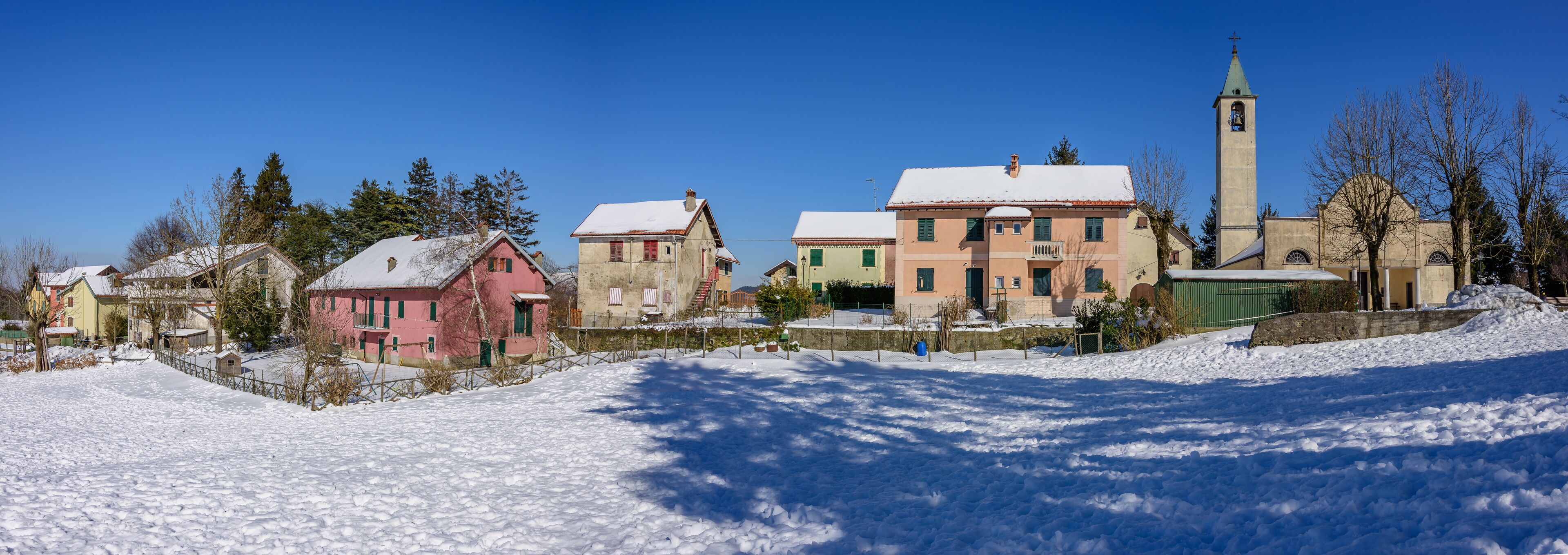 A snow-covered village with colorful houses, a church with a tall bell tower, and a clear blue sky.