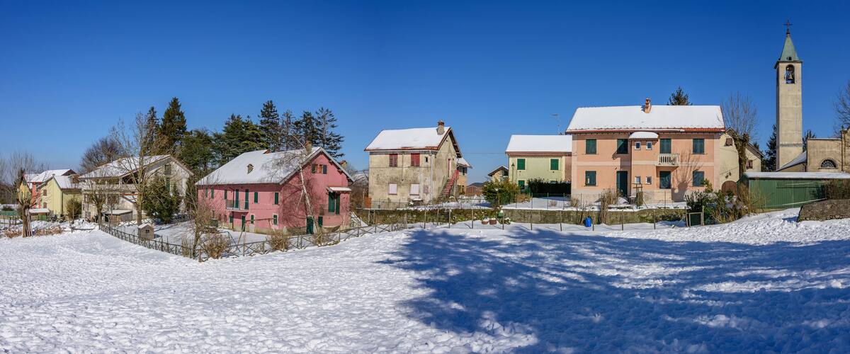A snow-covered village with colorful houses, a church with a tall bell tower, and a clear blue sky.