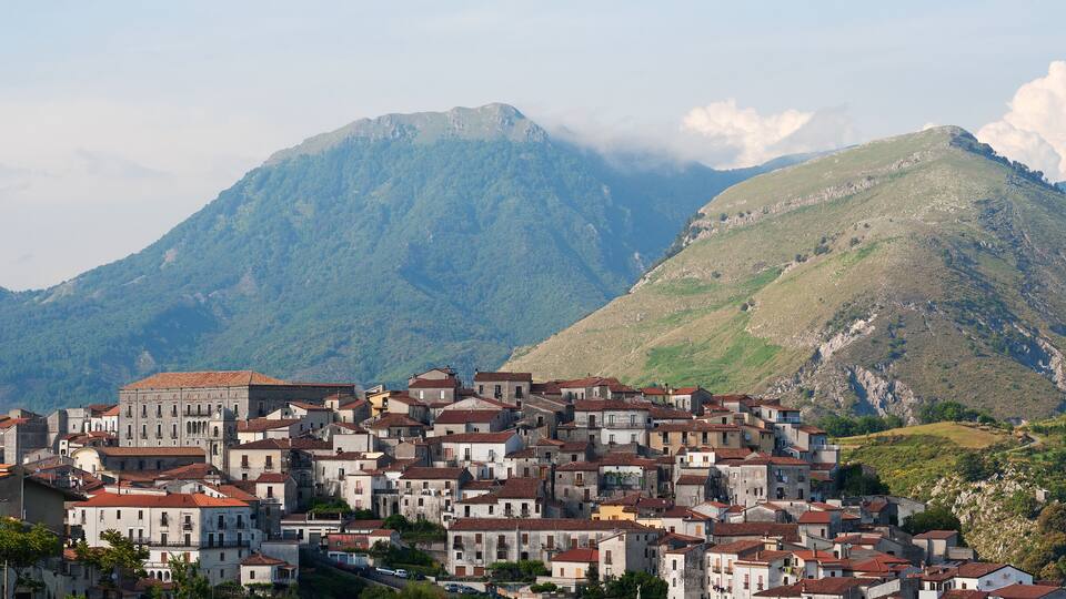A town with red-tiled roofs nestled against a mountain backdrop.