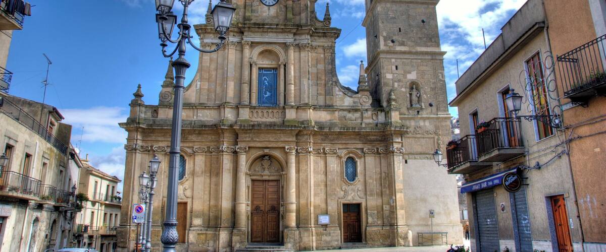 A historic church with a bell tower and a clock, surrounded by old buildings and a clear sky.