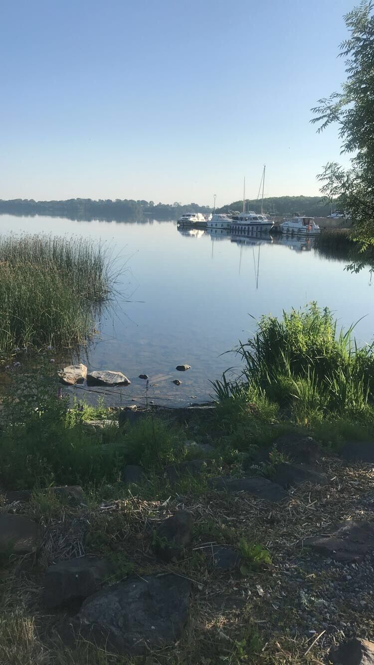 A calm lake with boats, grassy banks, and a clear sky.