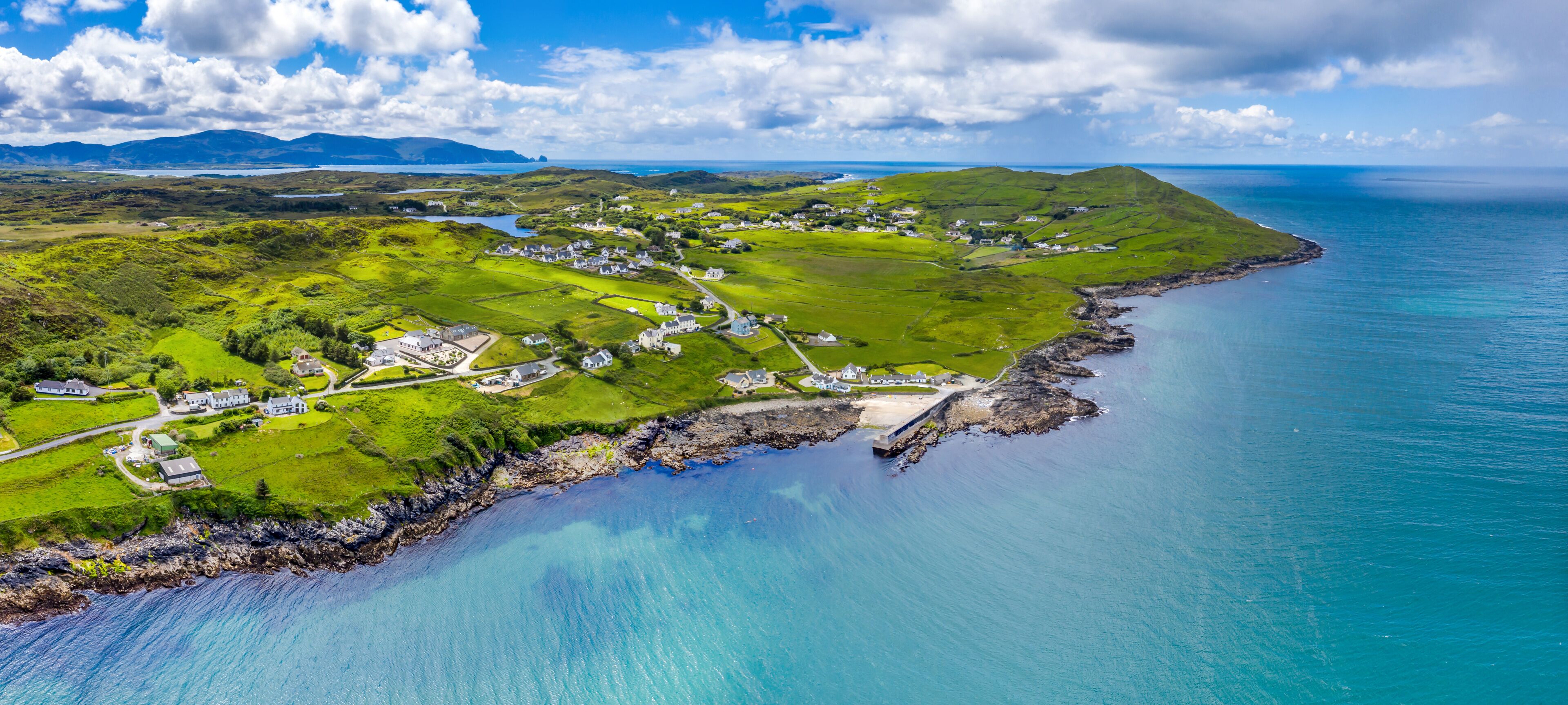 A coastal landscape with rolling hills, a small village, and a clear blue sea.