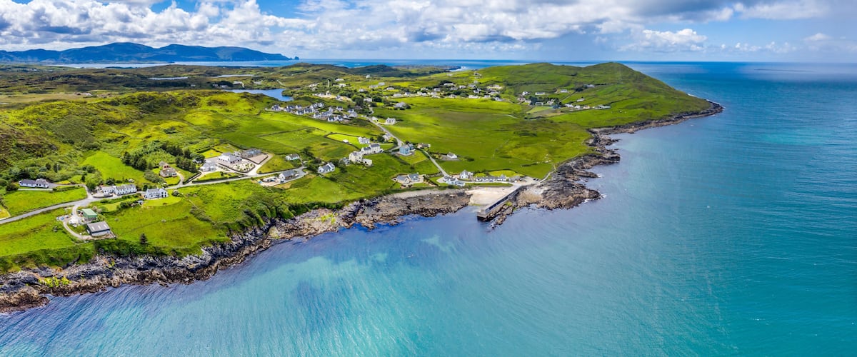 A coastal landscape with rolling hills, a small village, and a clear blue sea.