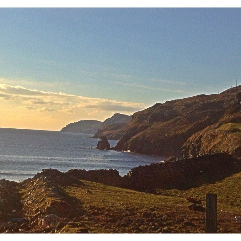 A coastal landscape with rocky terrain and a clear sky.