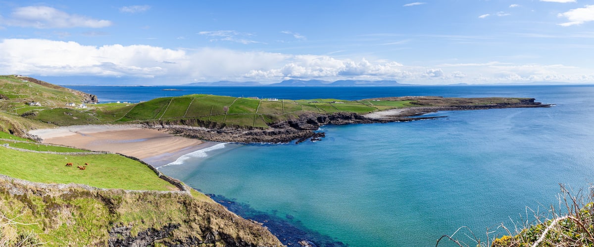 A coastal landscape with a beach, grassy fields, and a rocky shoreline.