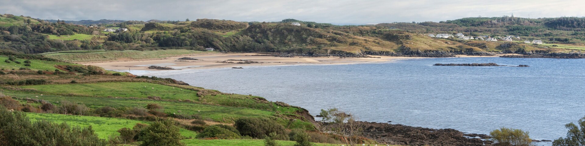 Un paisaje costero con colinas ondulantes, una playa arenosa y un mar tranquilo.