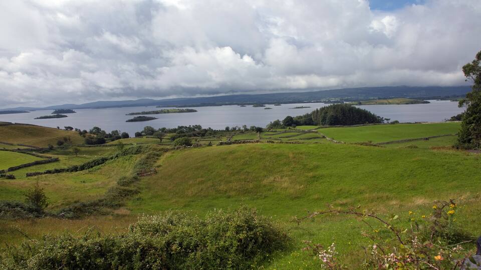 A coastal landscape with rolling hills, a large body of water, and distant islands.