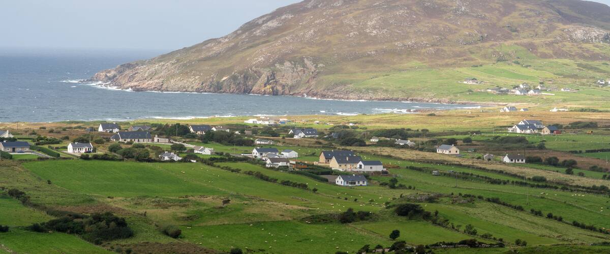 A coastal village with houses on rolling hills and a large mountain in the background.