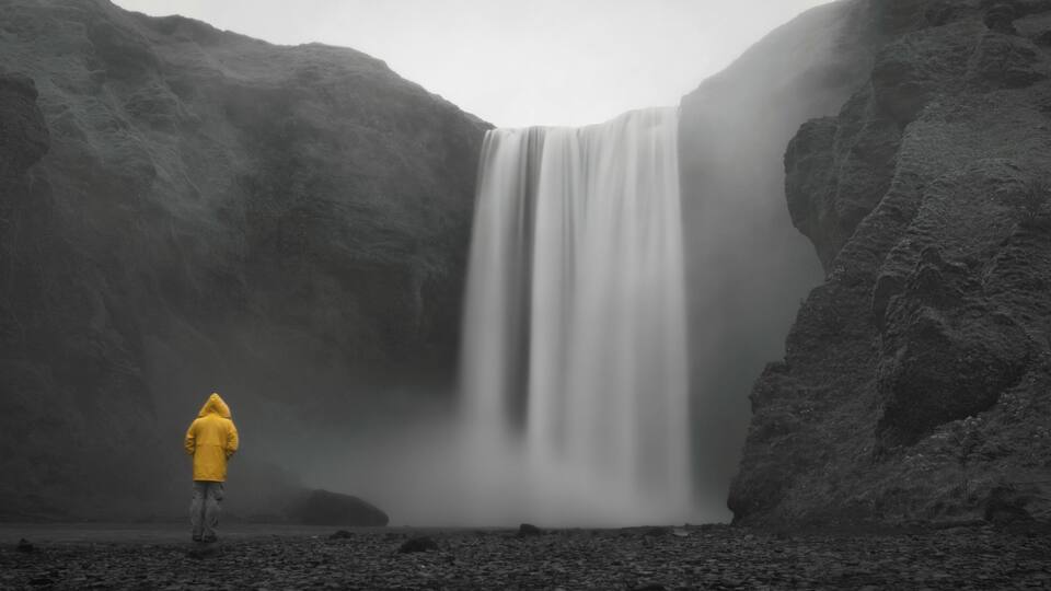 A person in a yellow jacket standing in front of a waterfall.