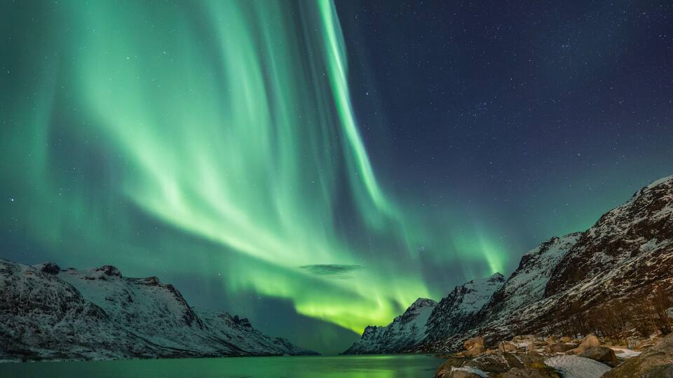A snowy mountain landscape with a lake and aurora borealis.
