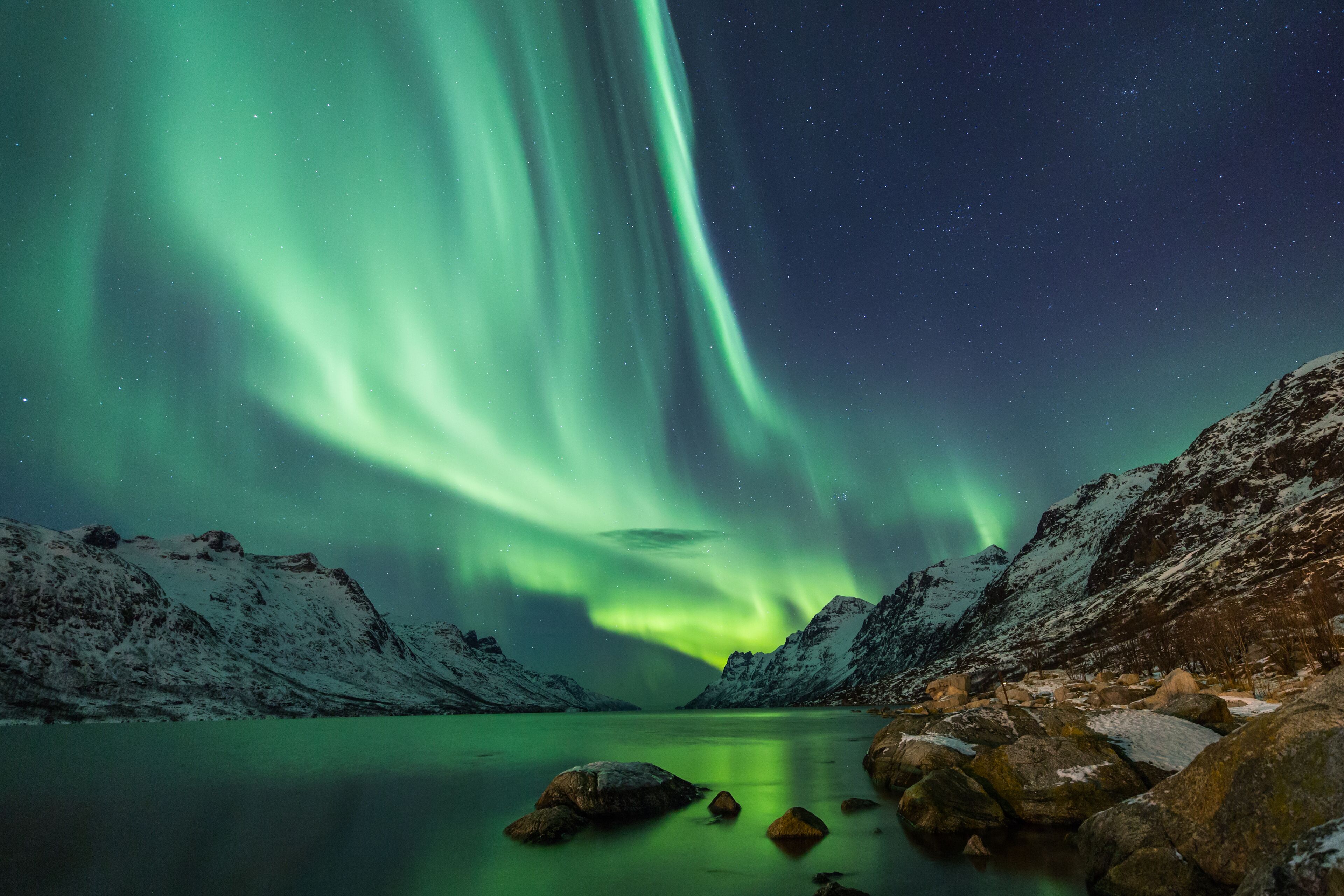 A snowy mountain landscape with a lake and aurora borealis.