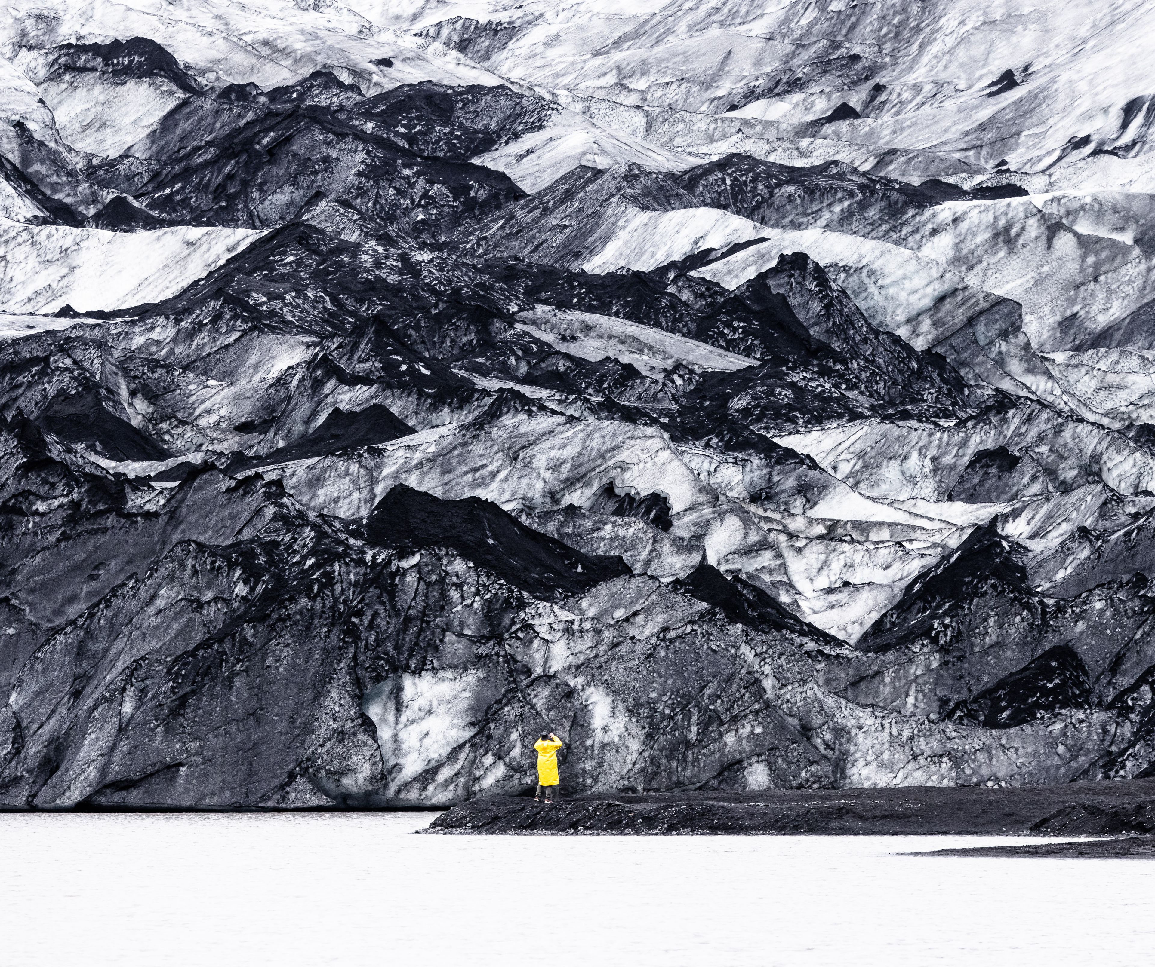tourist in yellow rain jacket in front of black and white landscape at Sólheimajökull Glacier in Iceland