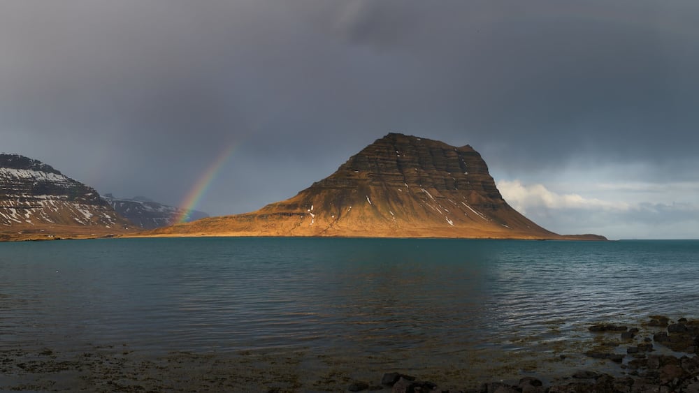 A coastal landscape with a prominent rock formation, a calm sea, and two rainbows.