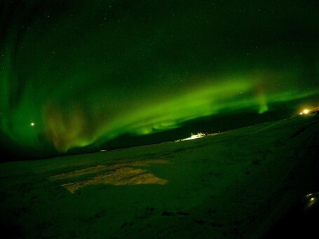 Nordlichter über einer verschneiten Landschaft mit einem abgelegenen Gebäude.
