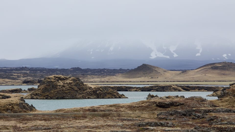 A rugged landscape with a body of water, rocky outcrops, and distant snow-capped mountains.