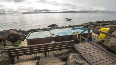 Un pontile in legno con vasche idromassaggio che si affaccia su una superficie d'acqua calma, circondato da rocce.