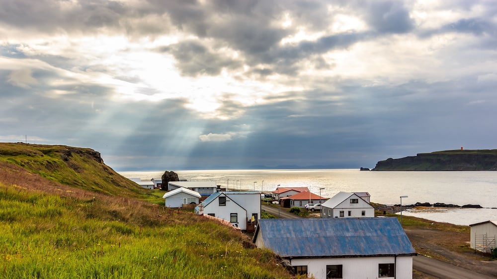 A coastal village with houses, a road, and a body of water under a cloudy sky.