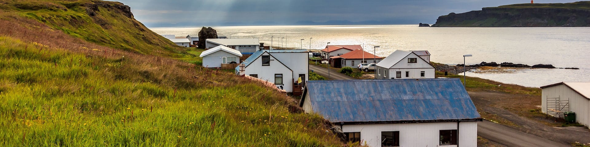 A coastal village with houses, a road, and a body of water under a cloudy sky.