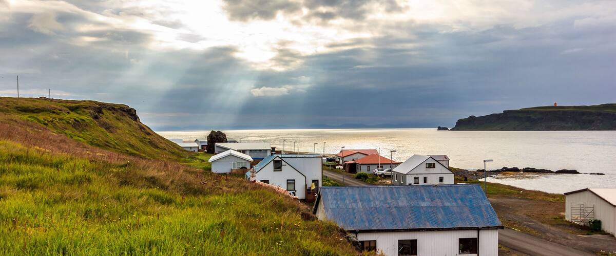 A coastal village with houses, a road, and a body of water under a cloudy sky.