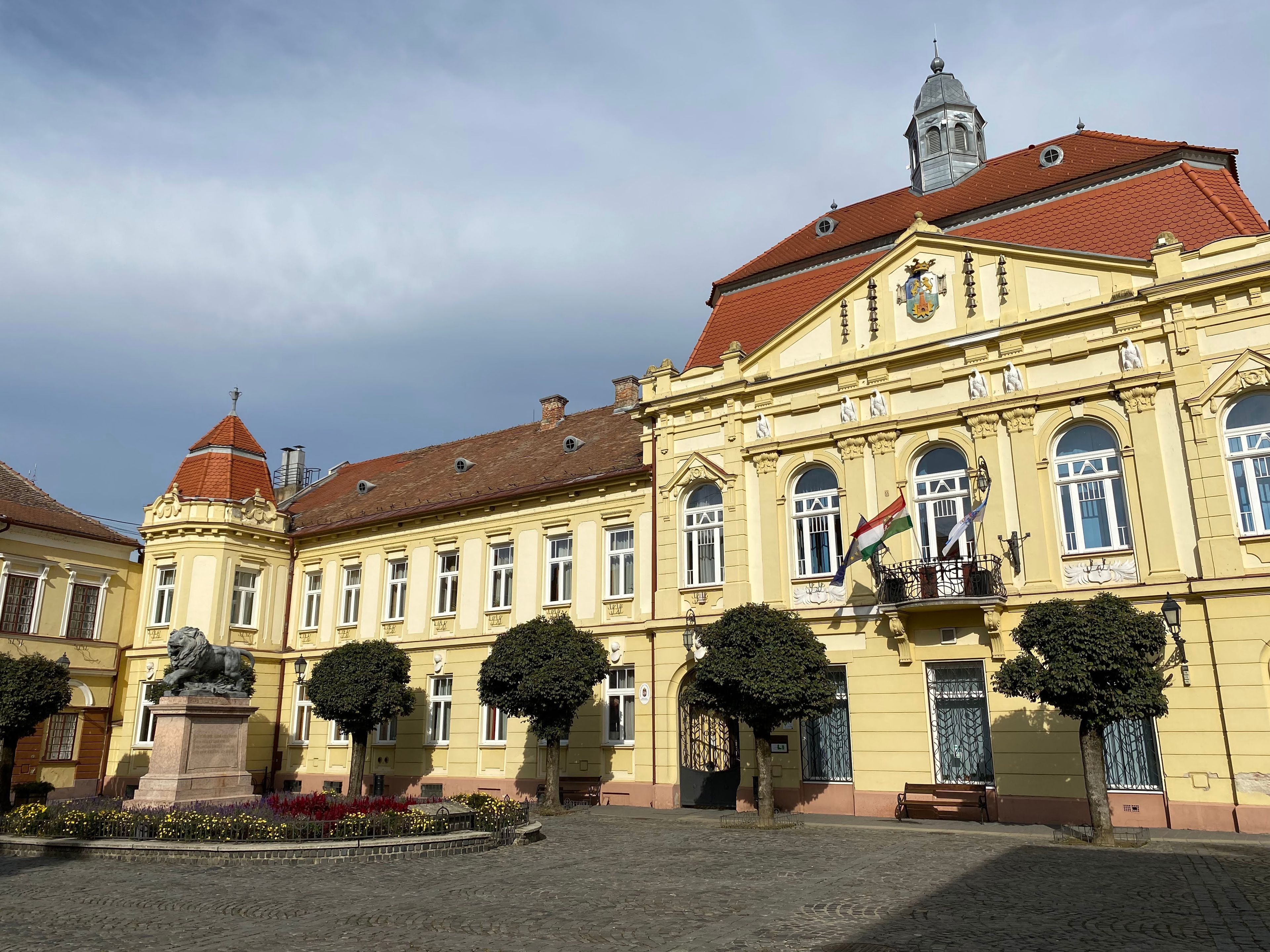 A historic building with a red-tiled roof, ornate facade, and a statue in the courtyard.