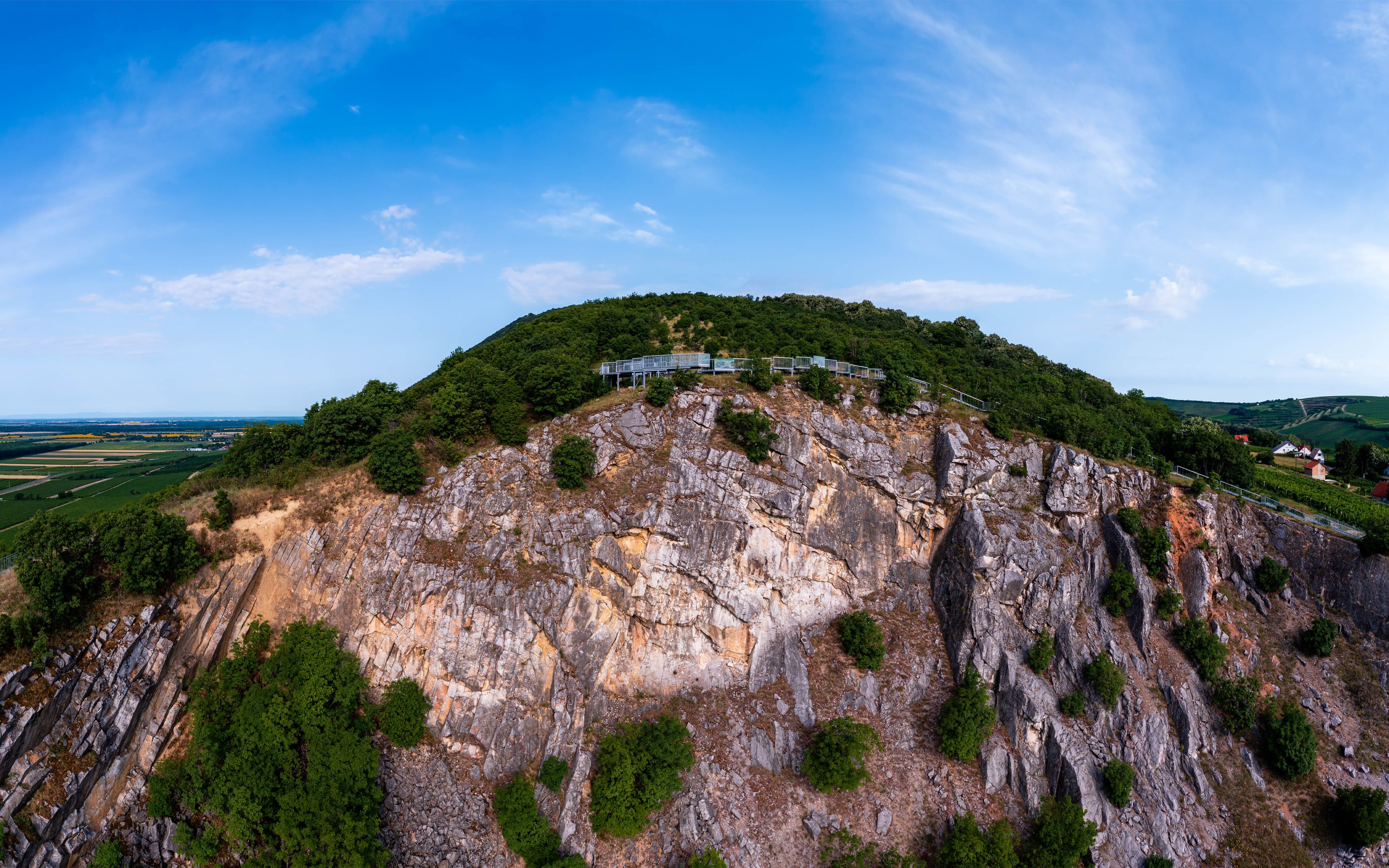 A mountainous landscape with a wooden walkway on top, surrounded by greenery and rocky terrain.