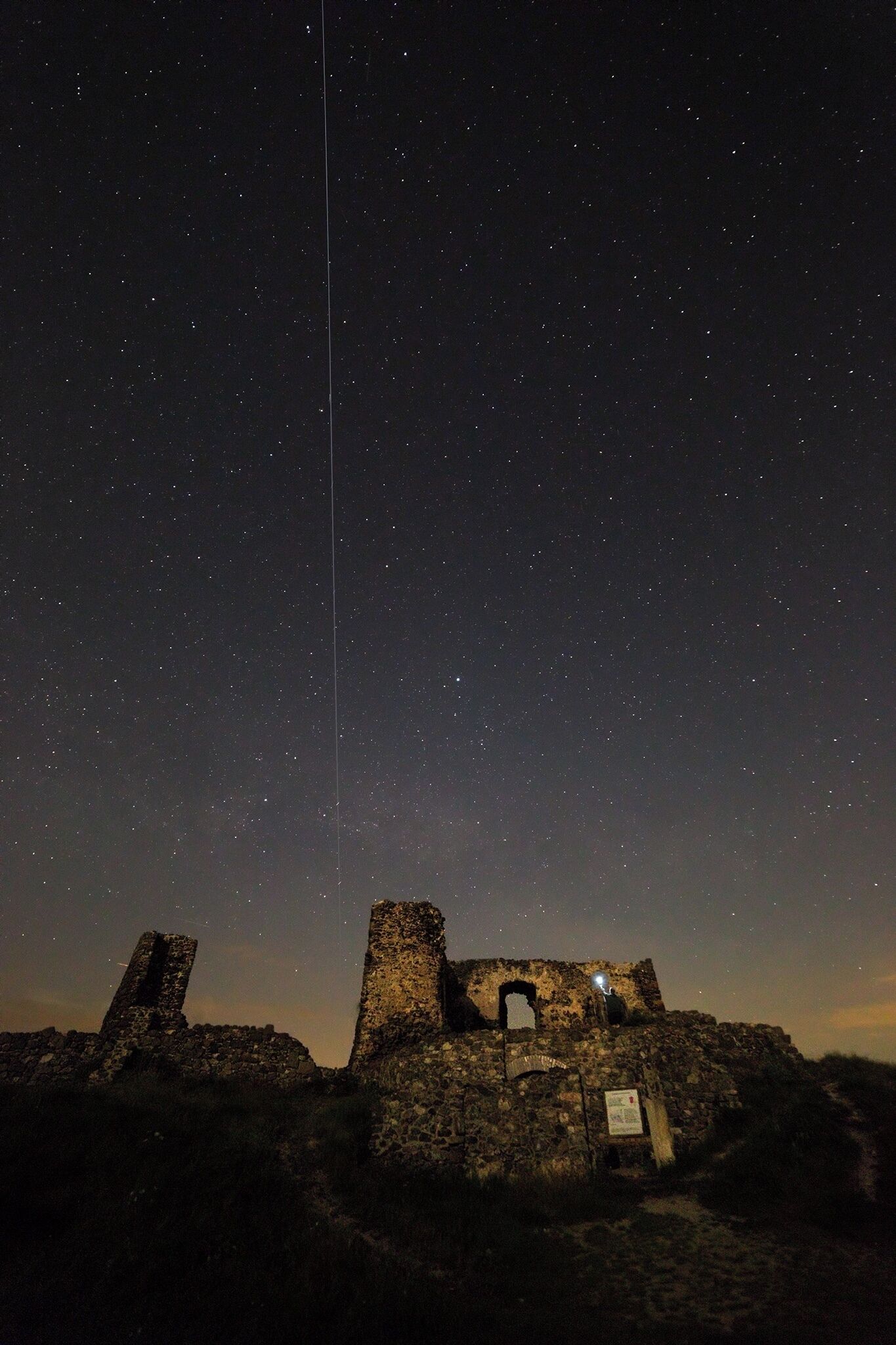 A starry night sky over ancient ruins with a tall, narrow tower.