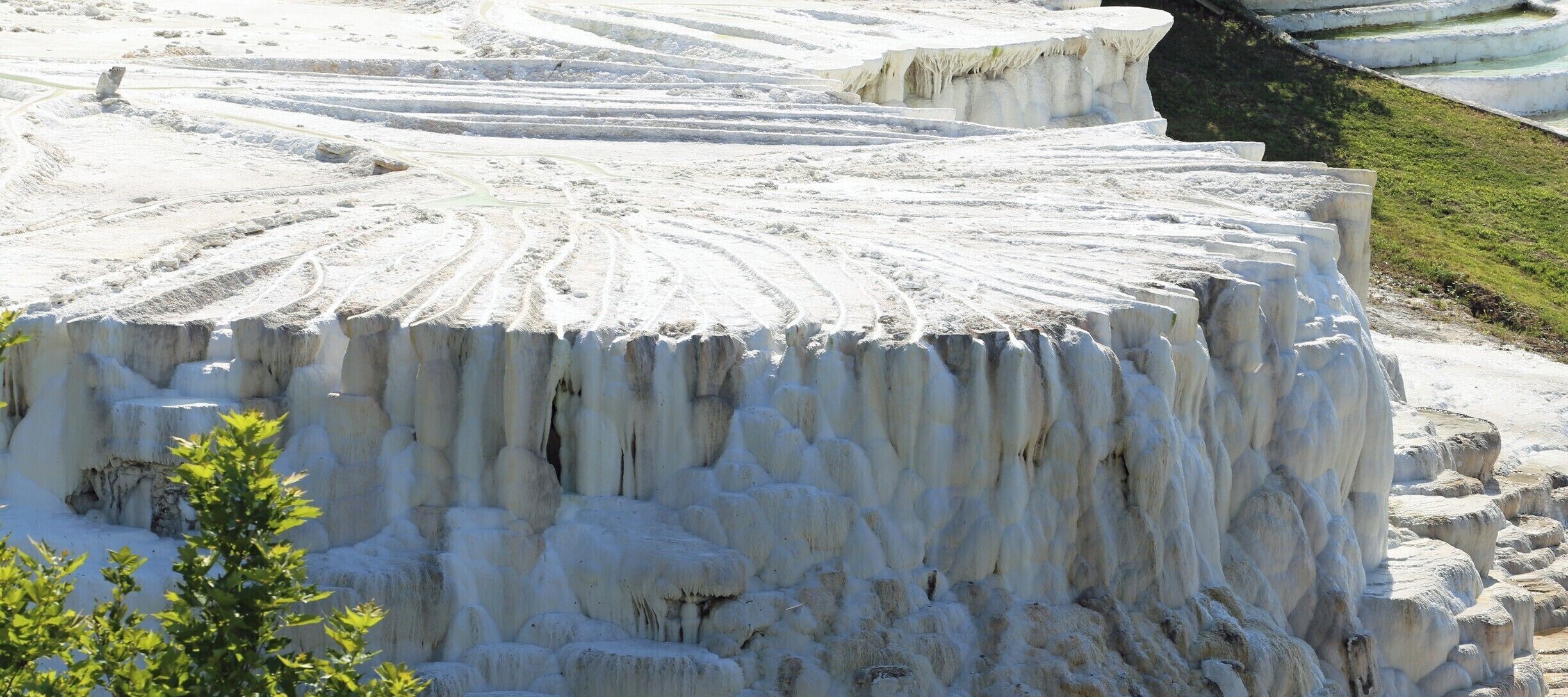 Terraced travertine formations with a circular pattern and a grassy area in the foreground.