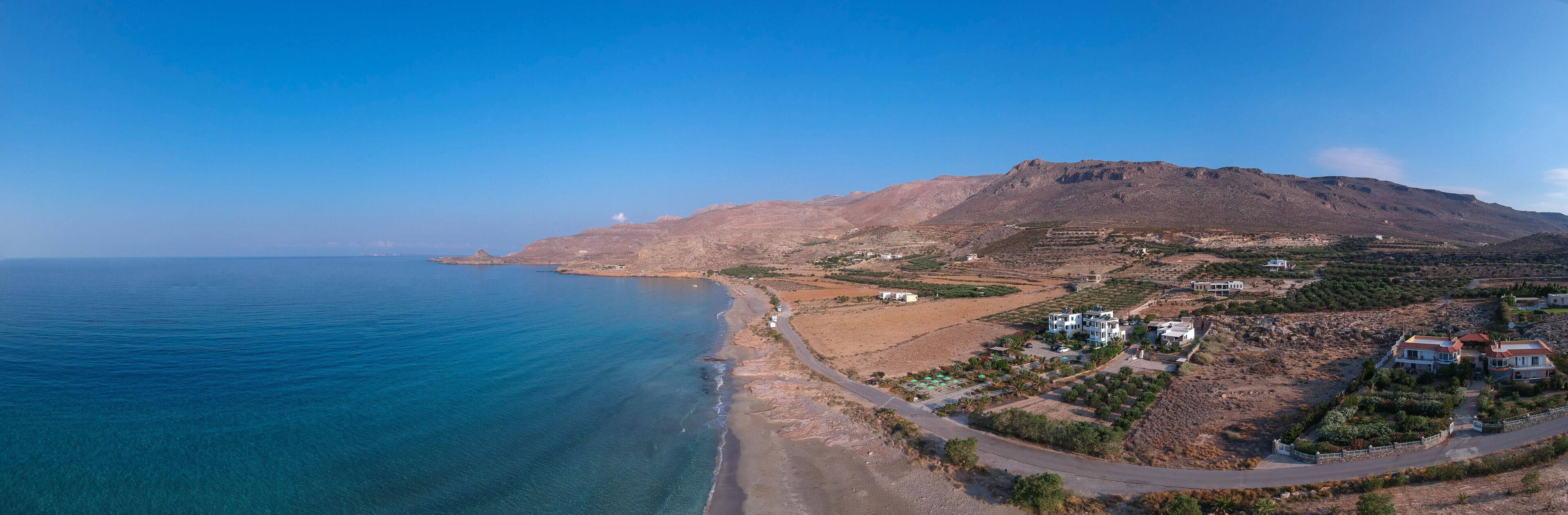 A coastal landscape with a mountain, clear blue sea, and scattered buildings.
