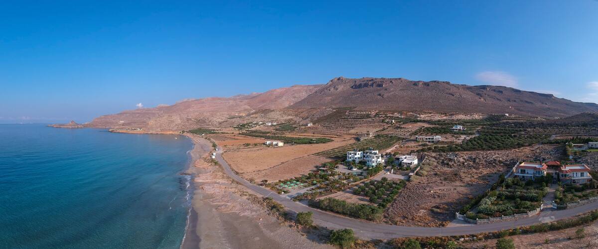A coastal landscape with a mountain, clear blue sea, and scattered buildings.