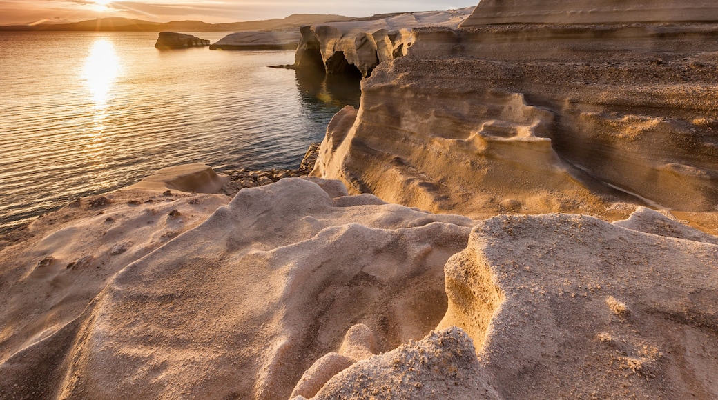 Eine Küstenlandschaft mit schichtartigen Felsformationen und einem ruhigen Meer bei Sonnenuntergang.