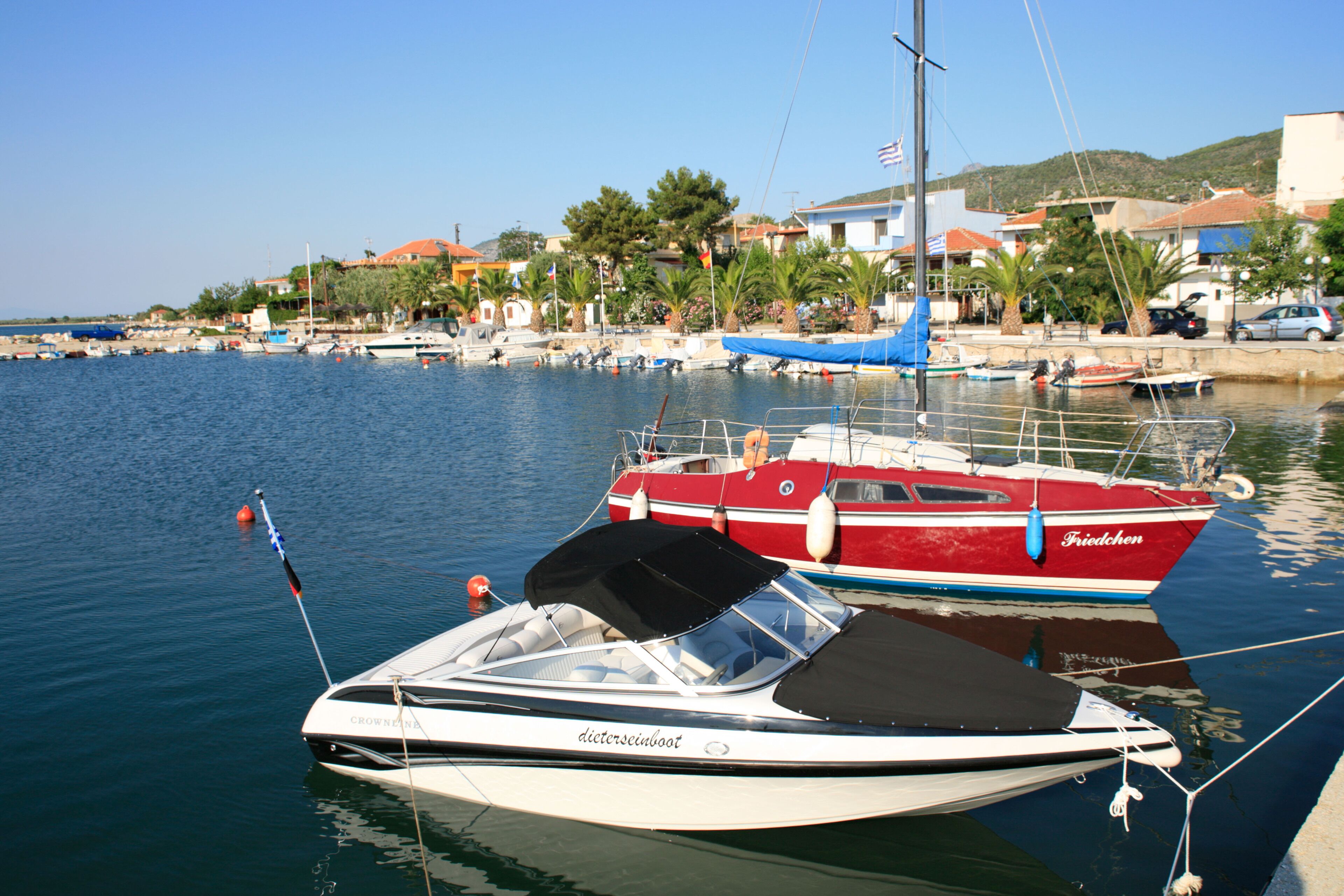 A marina with boats docked, a clear blue sky, and houses in the background.