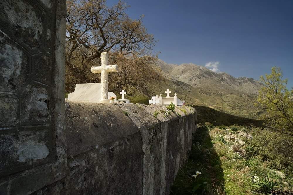 A cemetery with crosses and tombs, surrounded by mountains and sparse vegetation.