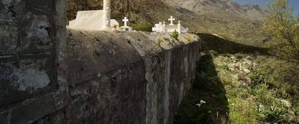 A cemetery with crosses and tombs, surrounded by mountains and sparse vegetation.