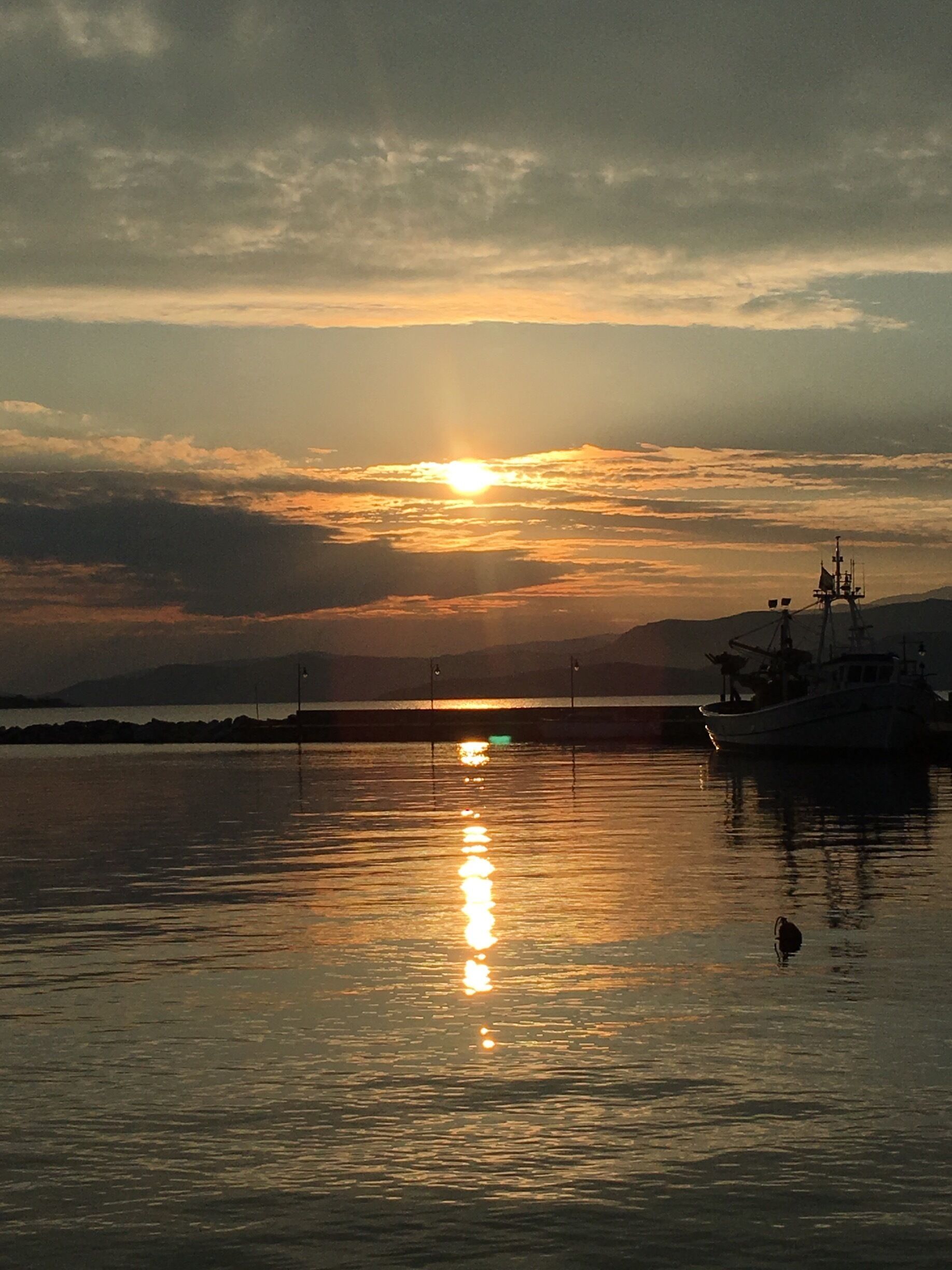 A sunset over a calm body of water with a boat and distant mountains.