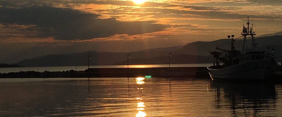 A sunset over a calm body of water with a boat and distant mountains.