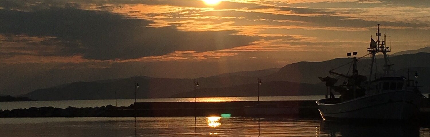 A sunset over a calm body of water with a boat and distant mountains.
