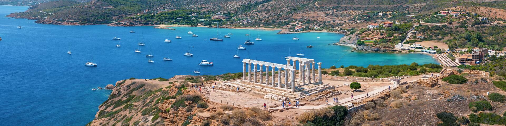 Panoramic view of the Temple of Poseidon at Cape Sounion at the edge of Attica, Greece, with moored sailboats in the bay during summer time