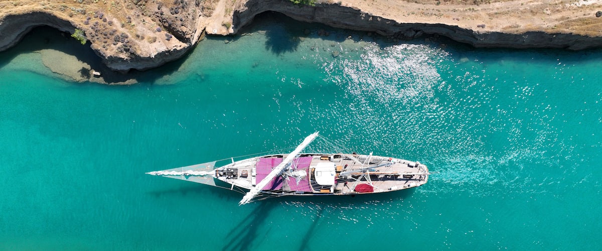A boat anchored in turquoise waters with rocky cliffs and dense greenery in the foreground.