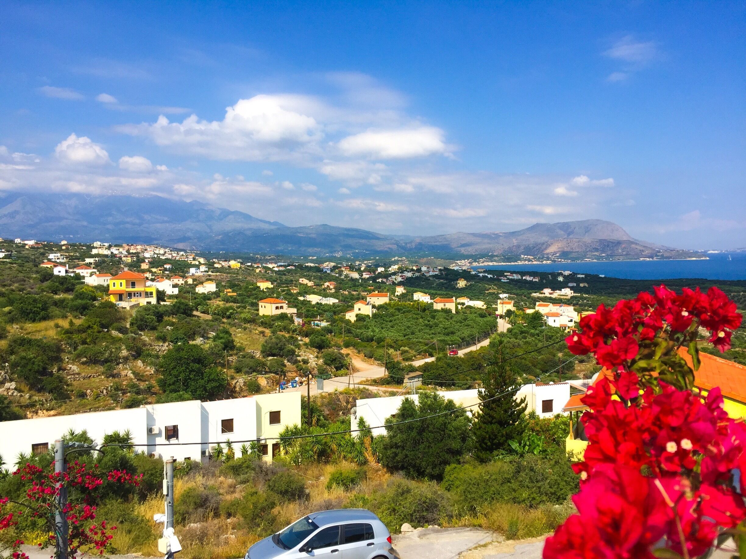 A coastal town with houses, a car, and mountains in the background.