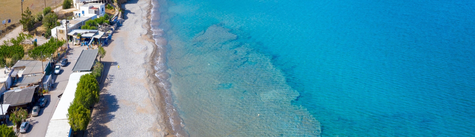 Un pueblo costero con mar azul turquesa, una playa arenosa y montañas al fondo.