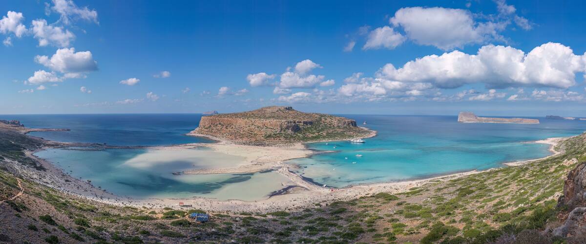 A coastal landscape with a prominent rocky island, clear turquoise waters, and a sandy beach.