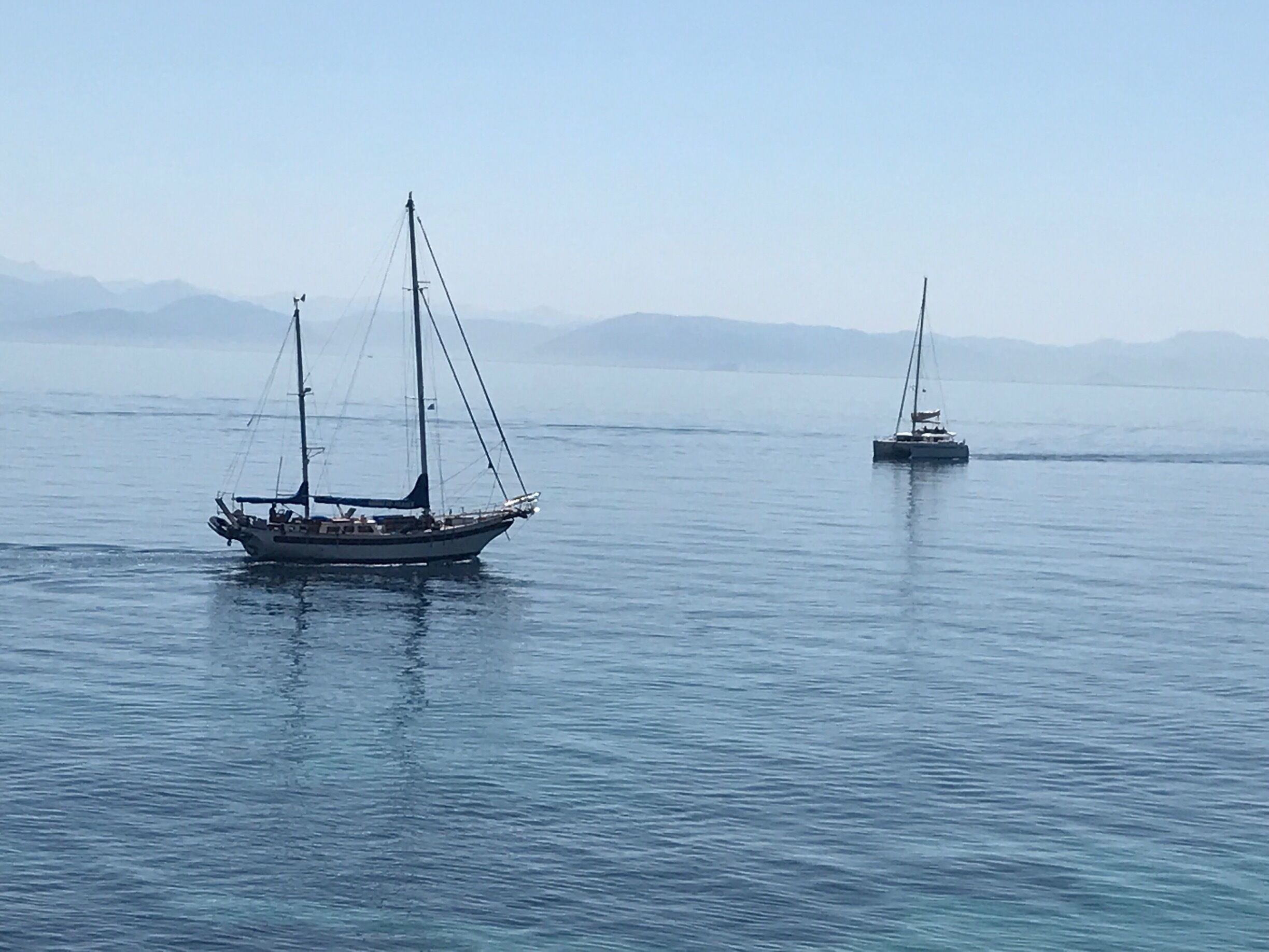 Two sailboats on calm water with distant mountains.