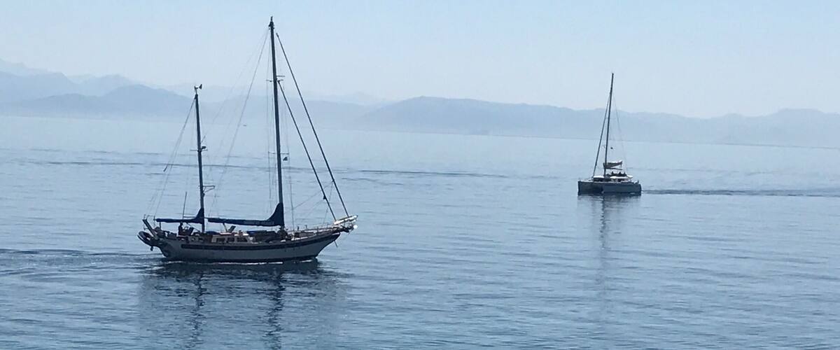 Two sailboats on calm water with distant mountains.